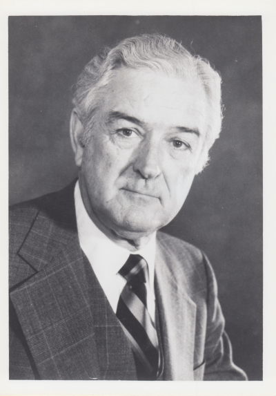 A black and white formal portrait of John Connally, a prominent American politician, looking directly at the camera. He is wearing a plaid suit jacket, a vest, and a striped tie.