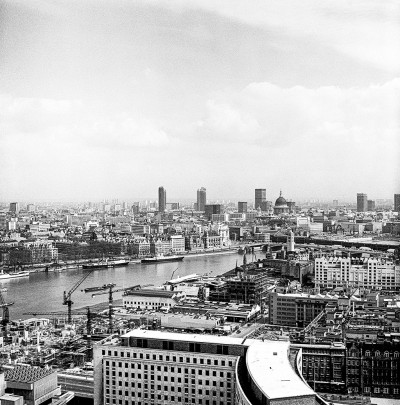 A black and white aerial photograph of the London skyline, taken in 1971. The River Thames flows horizontally through the middle ground, with St Paul's Cathedral dome and several early modern skyscrapers visible in the distance. Construction cranes and lower-rise buildings dominate the foreground and riverbanks, illustrating the city's development.